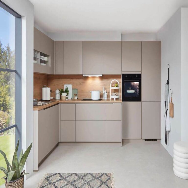 Musterküche in Kaschmir als L-Küche mit Holzrückwand und Backofen im Hochschrank – Küchenstudio Bergisch Gladbach